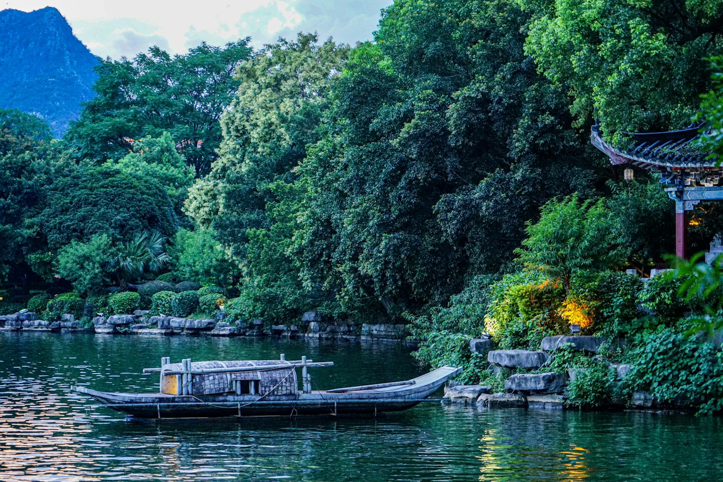 Barca di legno su un lago calmo che riflette alberi e montagna.