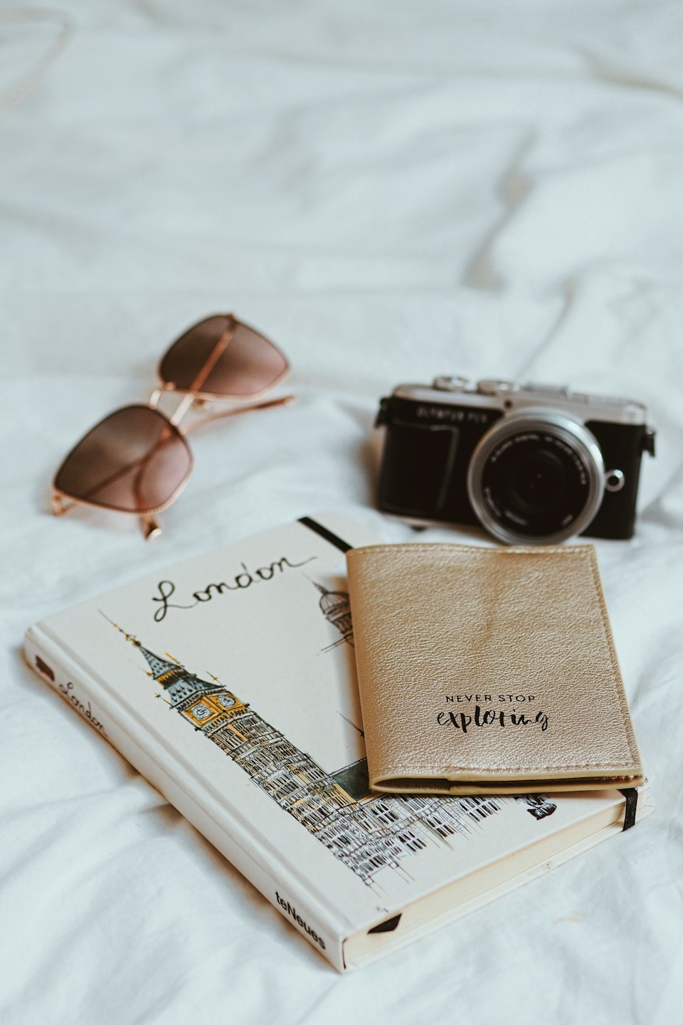 Necessaire da viaggio con taccuino, porta passaporto, occhiali da sole e macchina fotografica su lenzuola.