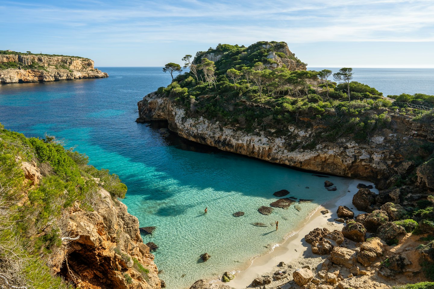 Due persone si rilassano su una spiaggia sabbiosa in una caletta costiera.